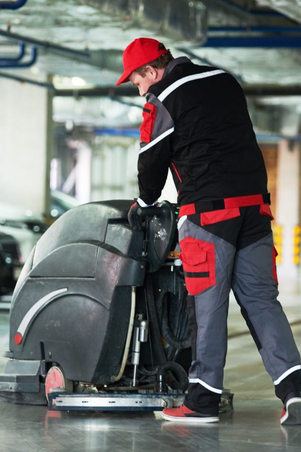 cleaning service. worker with machine cleaning floor in parking garage